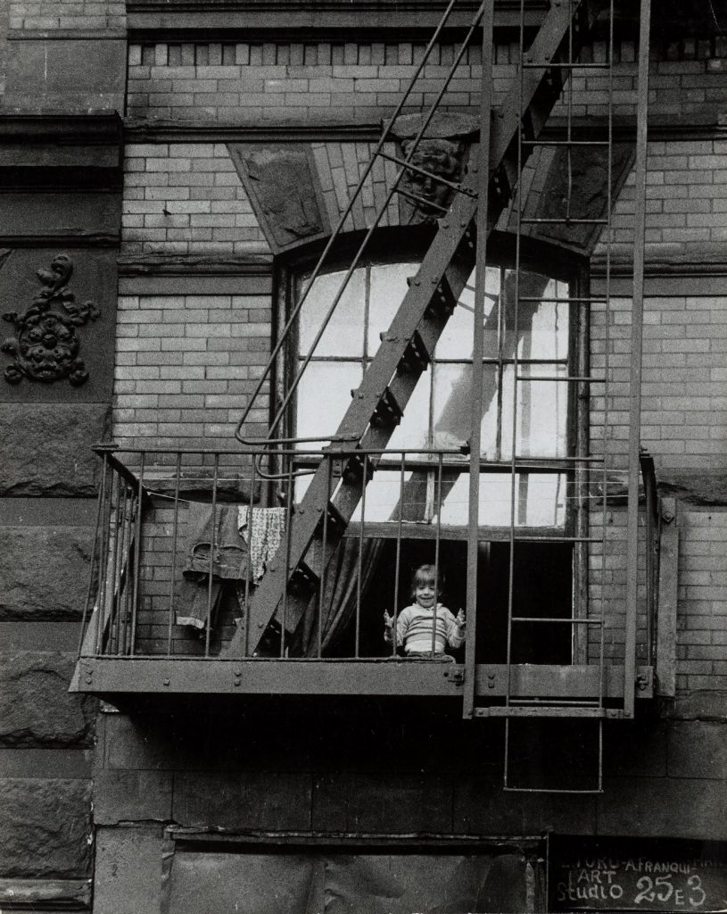 Old photo of a child in a window behind a fire escape.